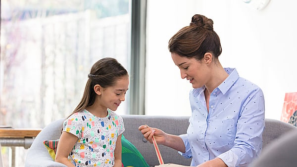 Woman and child sit on a sofa while unpacking a package together.